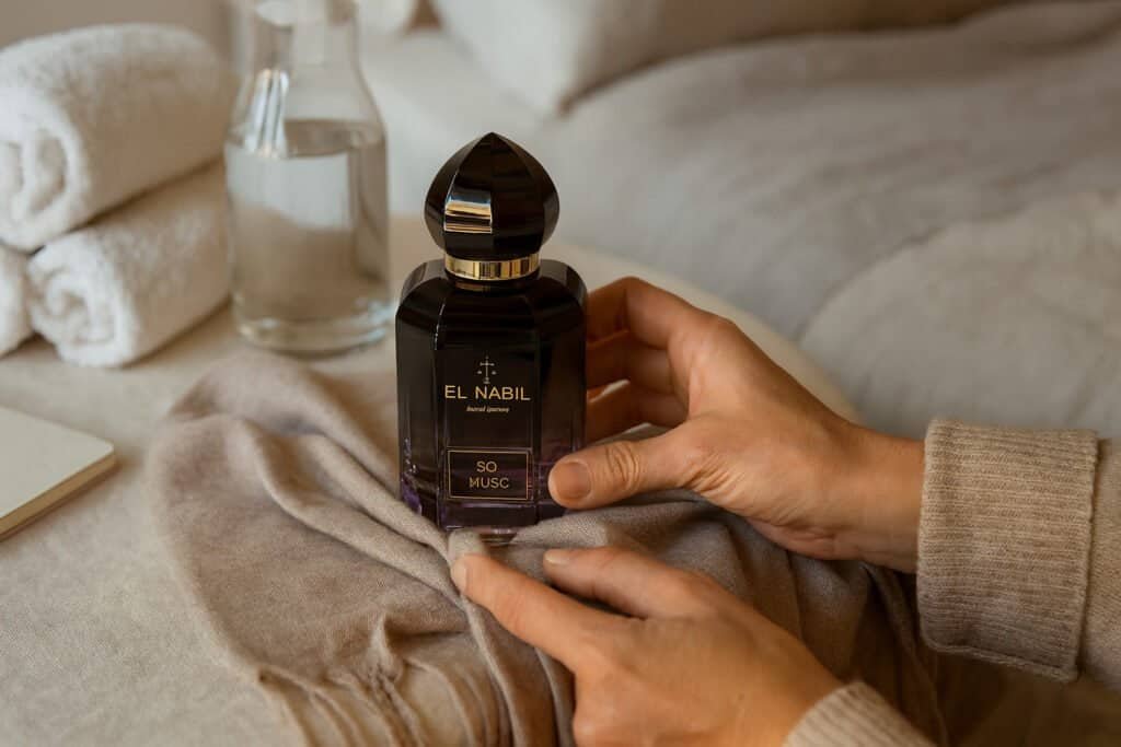 Mains préparant un rituel parfumé sur un plateau en lin blanc avec carnet, écharpe douce et lumière du matin